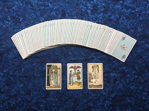 Tarot cards on a dark blue fabric background. Three are flipped upright and the rest are fanned in an arc above them.