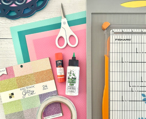 image of multicolored paper, scissors, tape, glue, and a paper cutter on a table