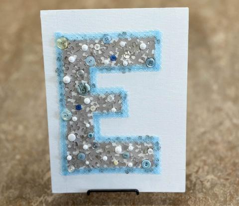 sample image of the letter E formed using mixed puzzle pieces, as well as lace, buttons, and beads.