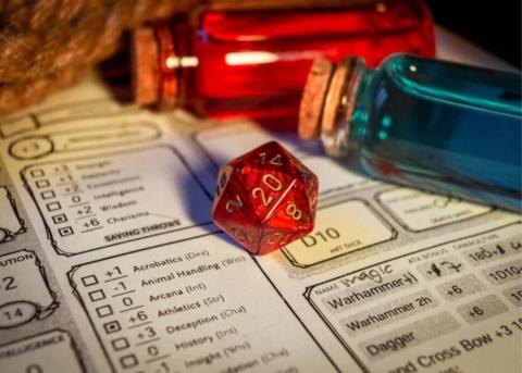 A D20 dice lays atop a player sheet, with two potion bottles (blue and red) laying next to it.