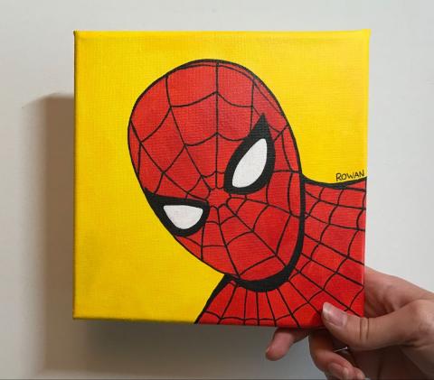 Hand holding a spiderman painting with yellow background