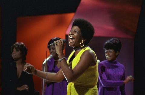 Aretha Franklin, backed by three singers in purple dresses, sings on stage