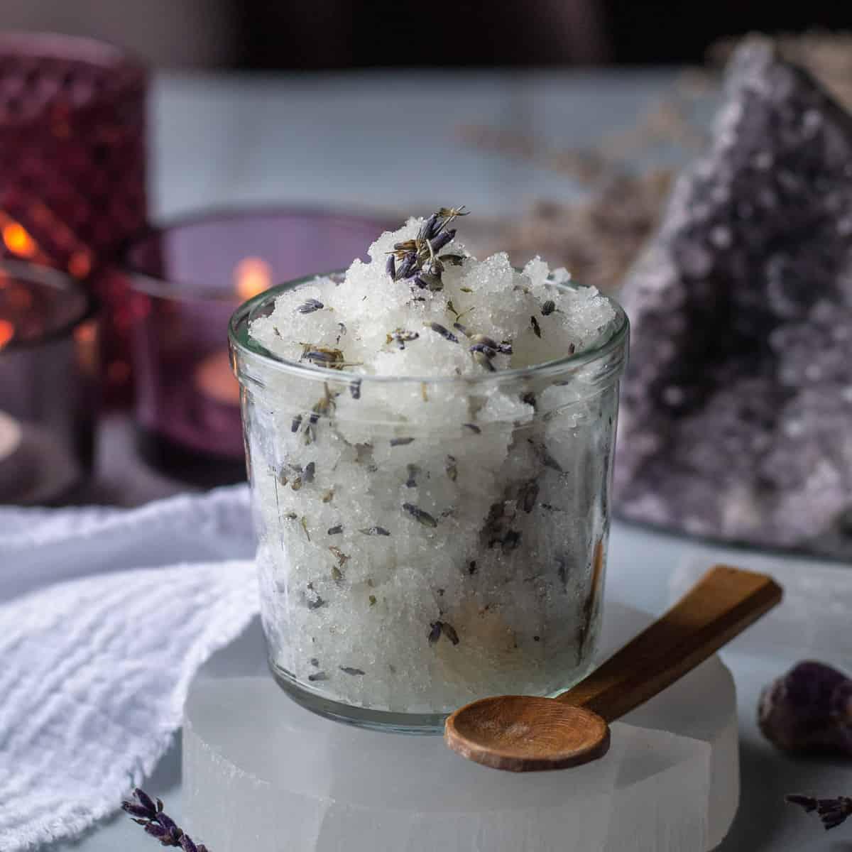 sugar scrub mixture in a glass jar with a spoon alongside it