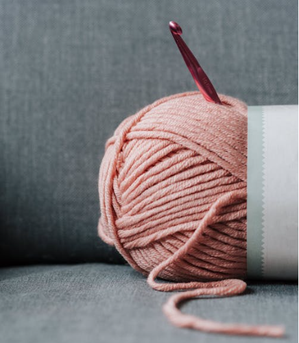 image of pink yarn with a pink crochet hook on a gray background