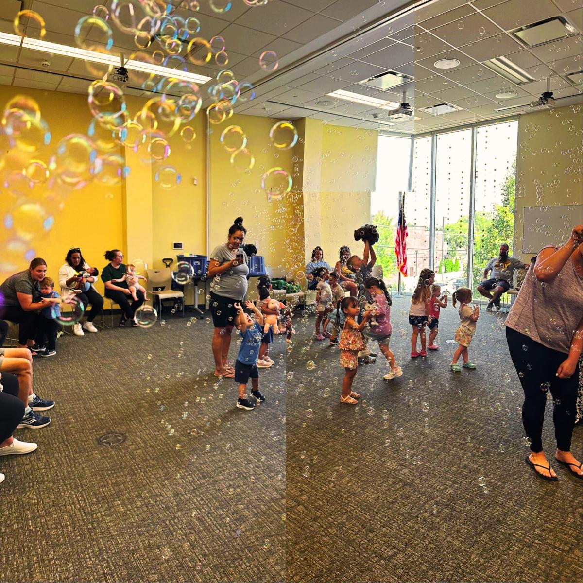 Lot of adults and children gather around dancing and popping bubbles floating through the air. Around the edge of the picture some adults and children sit and enjoy the bubbles and music.