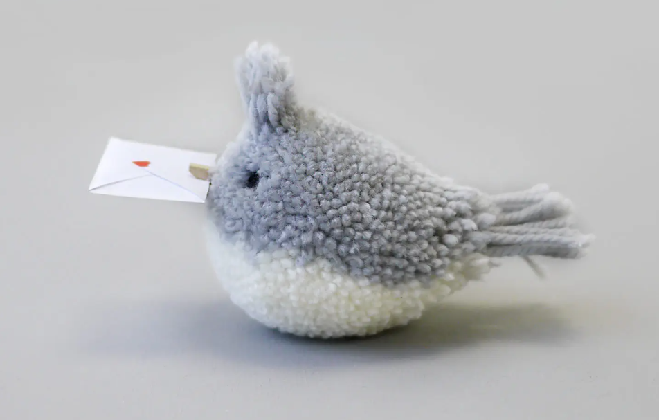 gray and white pom pom bird with a tiny valentine envelope in its beak