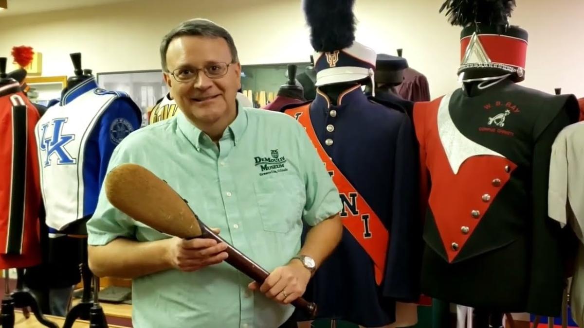 smiling man standing in front of uniforms holding a paddle